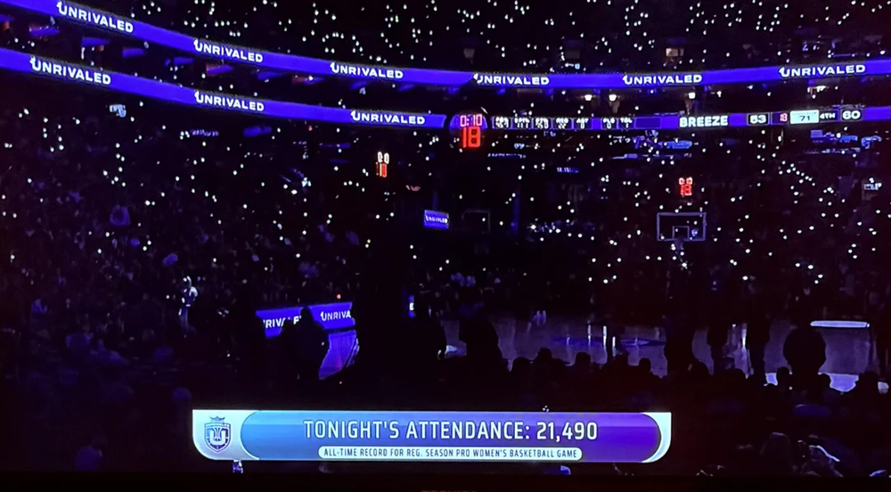 Source: Reddit. Lights out in the arena only the spec of lights from hand holding and the unrivaled marquee in purple and white. This is a screen grab from the stream with banner at the bottom saying "Tonight's attendance: 21,490" .